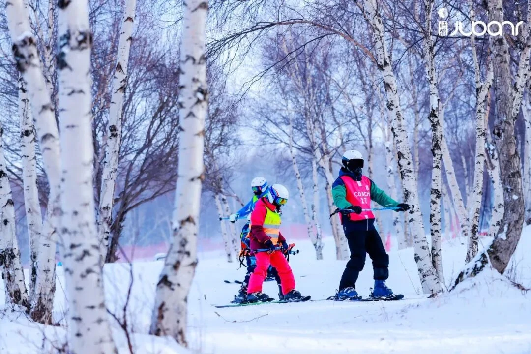 桔瓣滑雪营教练与孩子在雪林里一起滑行